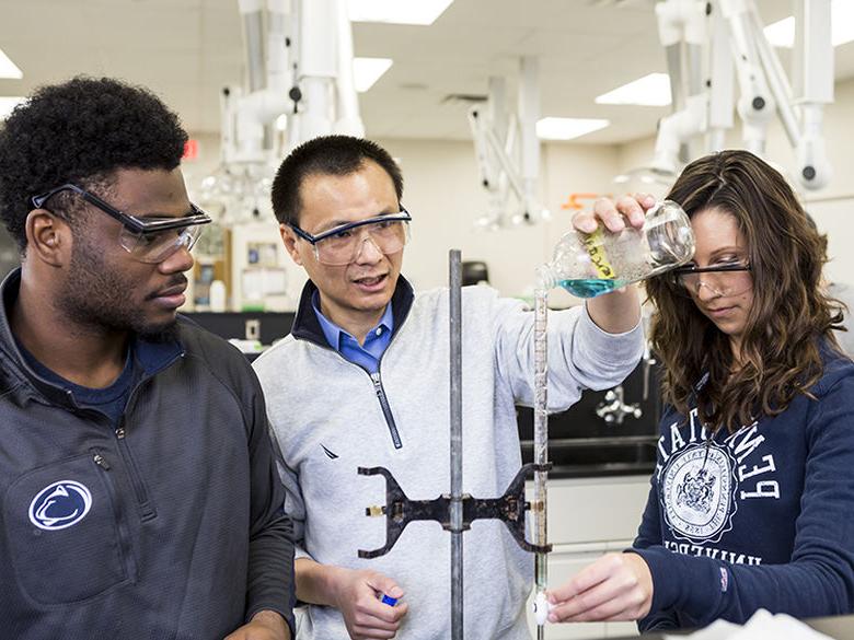 一名女学生和一名男学生在化学实验室里和他们的老师一起工作